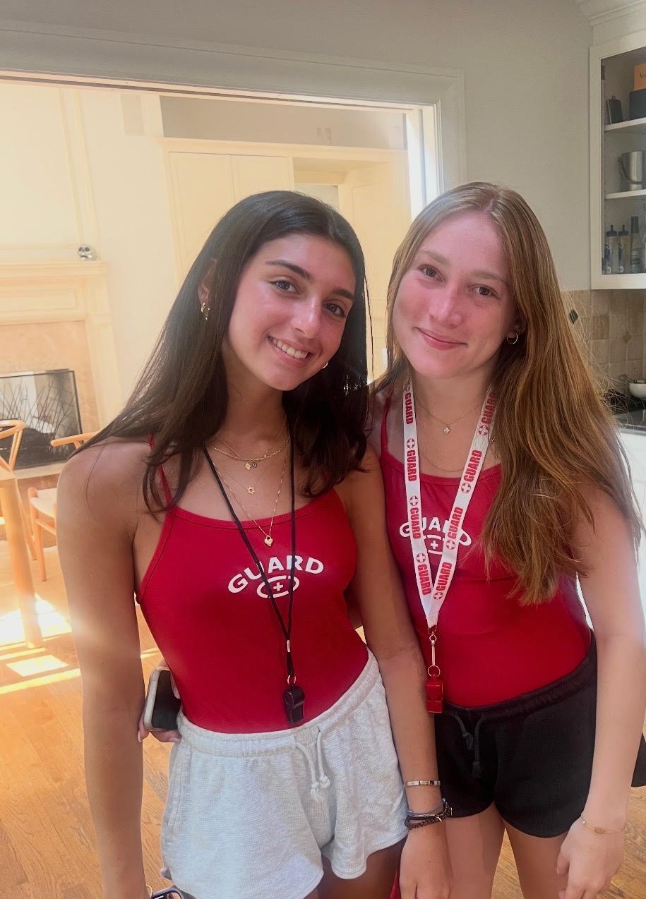 Elle with a fellow certified lifeguard, both in red guard uniforms with whistles